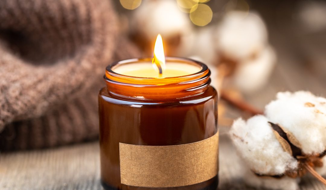 A burning candle with a few burnt matches nearby and a piece of cotton. There is also a sweater behind the candle.