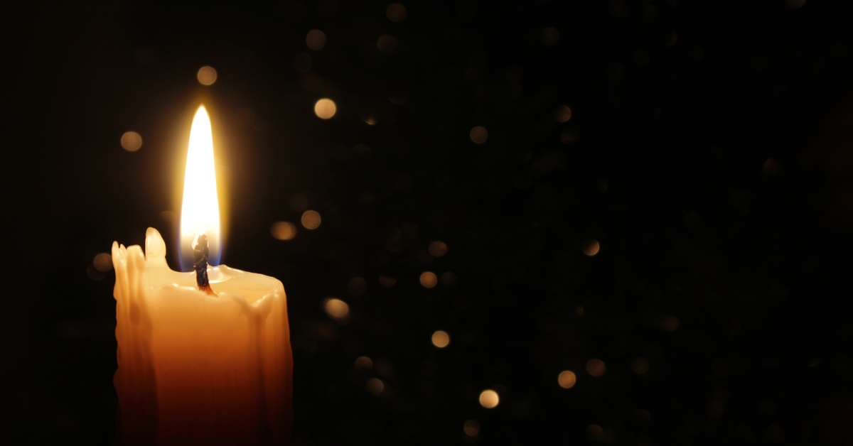 A lit candle in a pitch-black room. The edges of the candle are a bit jagged, and there are some sparks floating around.