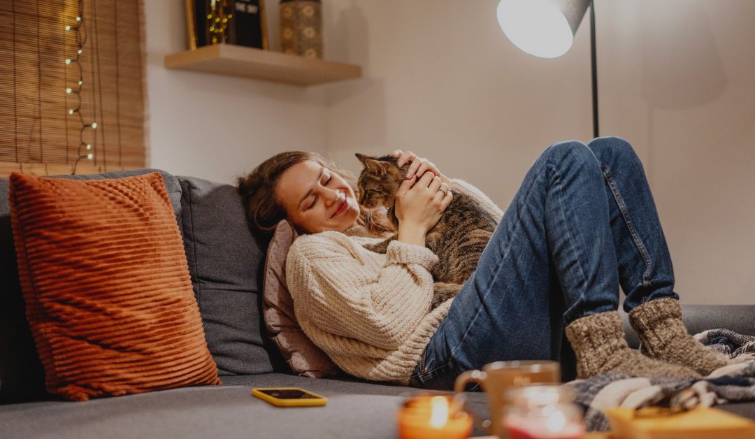 A woman relaxing on a sofa while holding a tabby cat near warm candlelight and soft evening home decor.