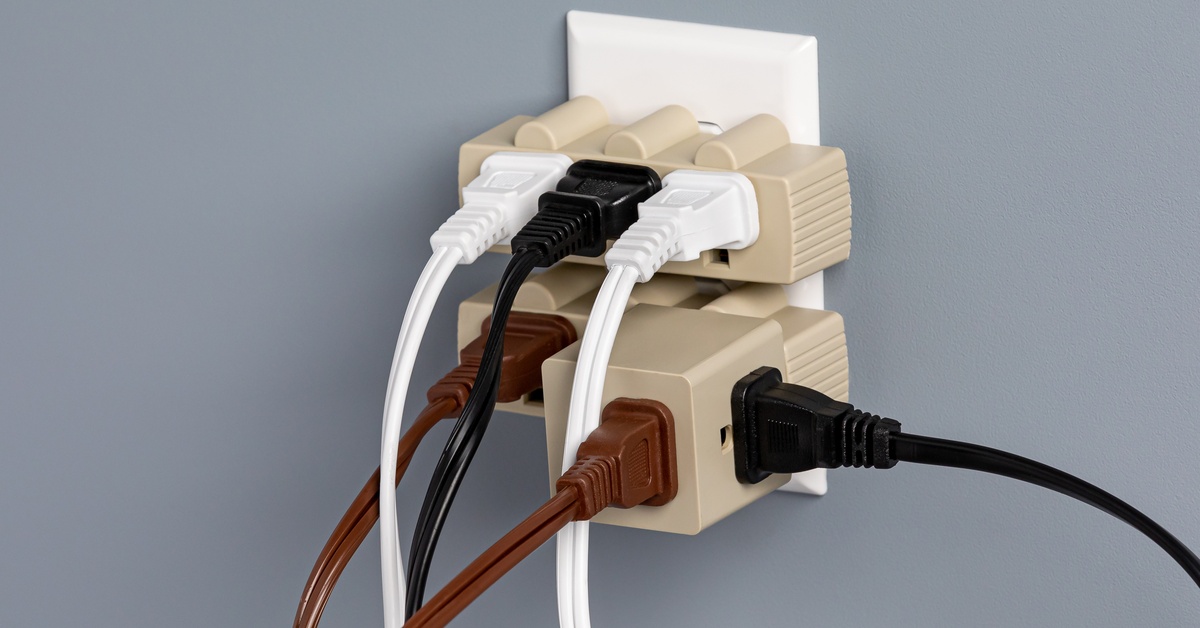An electrical outlet that's been overloaded with splitters. There are multiple cords plugged into these splitters.