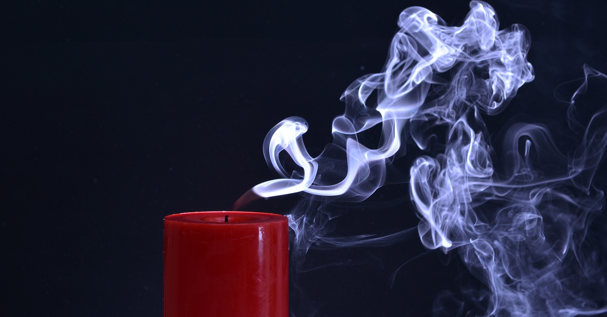 A red candle in a dark room that had its flame blown out. There is a lot of smoke coming from the candle.