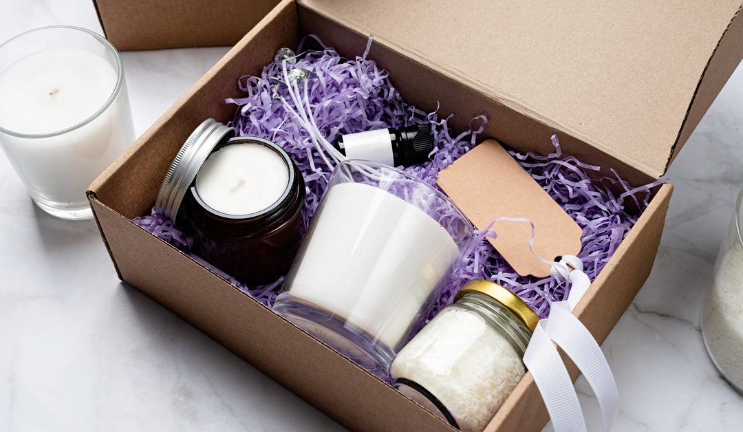 A DIY candle gift box with wax, a jar candle, and essential oil. There is another candle sitting outside the box.