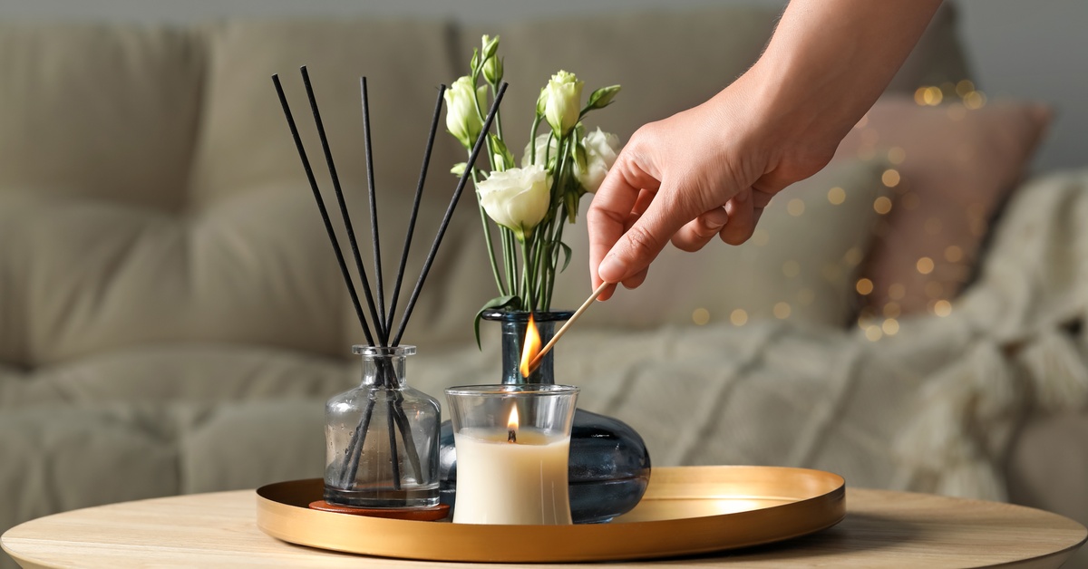 A woman lighting a candle on a wooden table in a living room with a light green couch in the background.