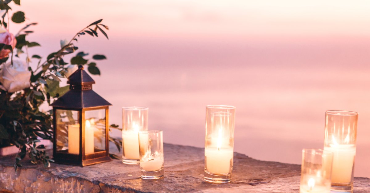 Candles and flowers are arranged as evening decorations on a stone wall overlooking a large body of water.
