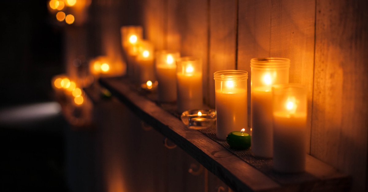 A small wooden shelf with multiple candles of different types. There are hooks for coats underneath the shelf.