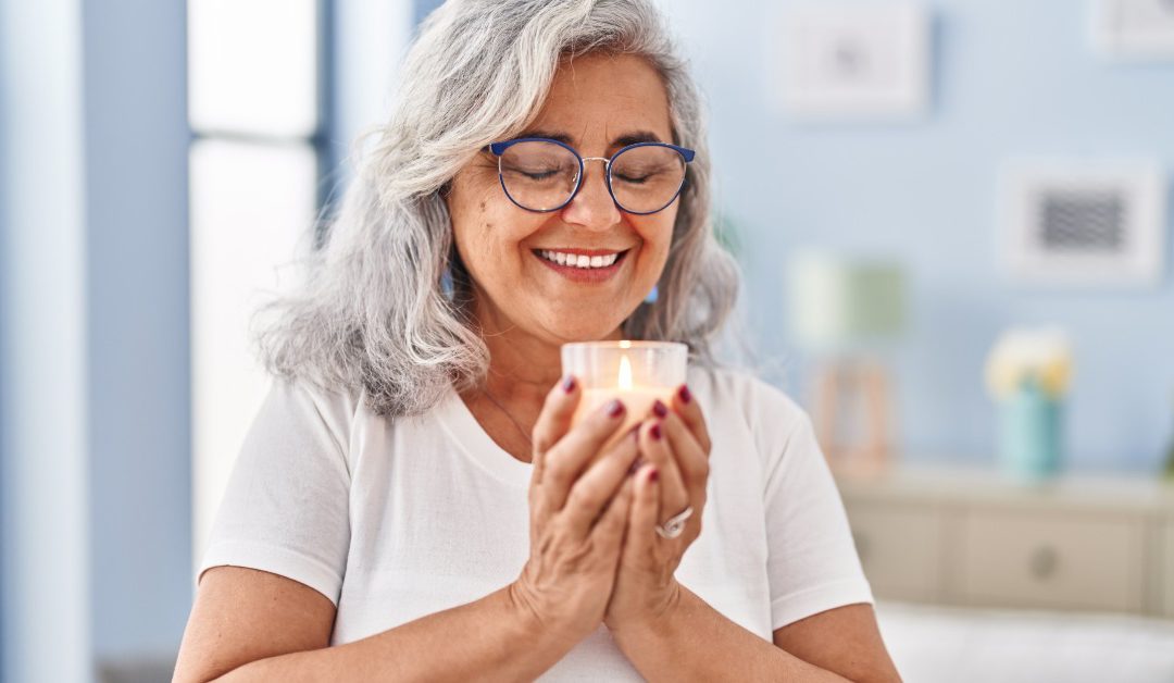 A woman standing while smelling an aromatic candle, with soft indoor light and a calm living room background.
