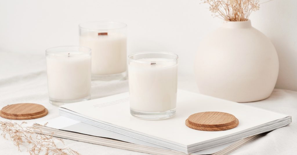 Candles in glass containers with wooden lids and wooden wicks sitting together on a plain white surface.