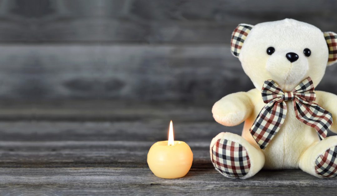 A teddy bear sitting beside a small white candle on a wooden surface, with open space across the background.