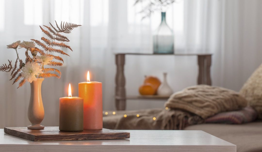 A pair of candles burning on the coffee table next to a vase with faux florals. There's a couch behind the table.