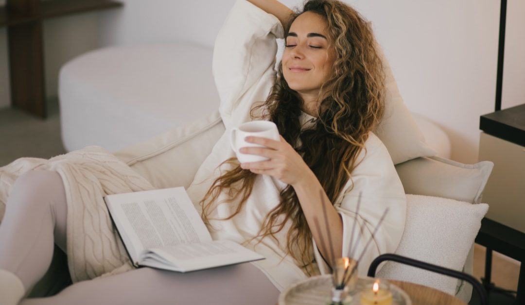 A young woman comfortable at home kicked back on her accent chair. A small tray with candles sits next to her.