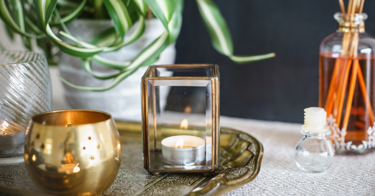 Candles, a reed diffuser, a plant, and framed art arranged together as vintage-style home decor on a table.