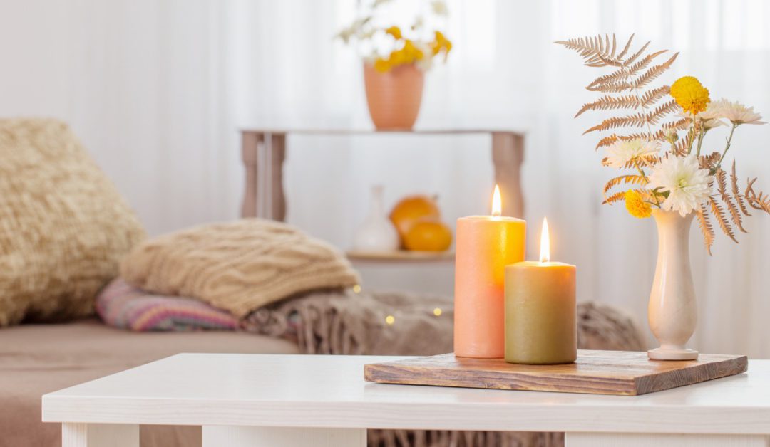 Burning candles arranged with autumn decor on a white table, casting warm light into the living room.