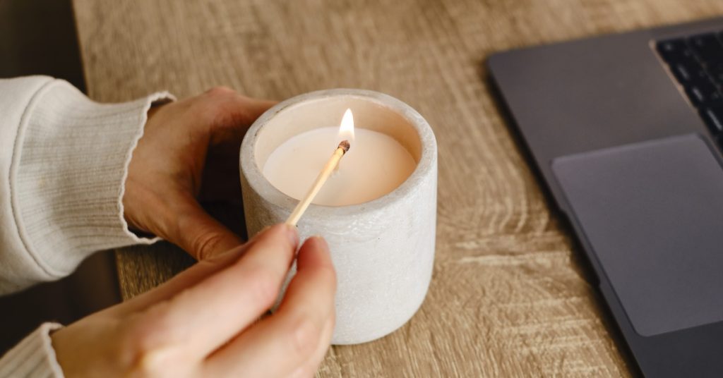 A close-up of someone lighting a candle with a match. The table is wood and there's a laptop close by.