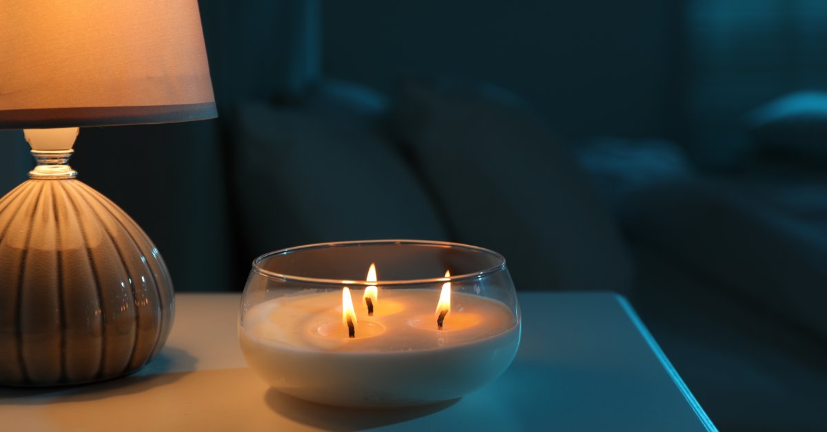 A large glass candle with three wicks burns on the nightstand with a smaller lamp lit up behind it.