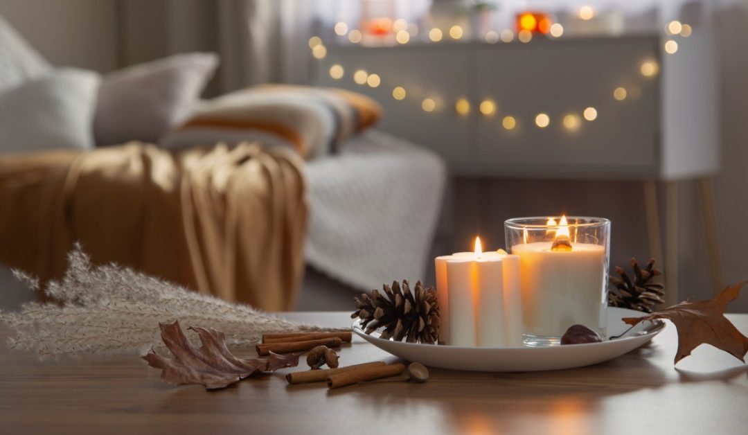 A small tray sits on a table with two burning pillar candles. There are pinecones and autumnal leaves close to the tray.