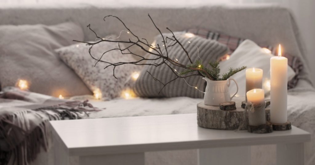 A cozy living room with a white, modern coffee table. The table has three various-sized pillar candles burning.