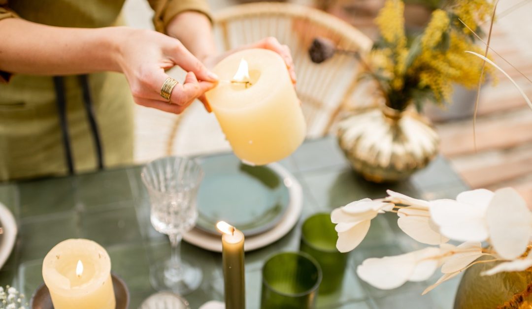 A close-up of a homeowner lighting a candle as they set the outdoor dining table. There are pillar and taper candles.