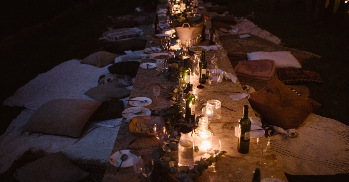 An outdoor dining arrangement at nighttime with pillows for seats on the sides. There are candles as centerpieces.