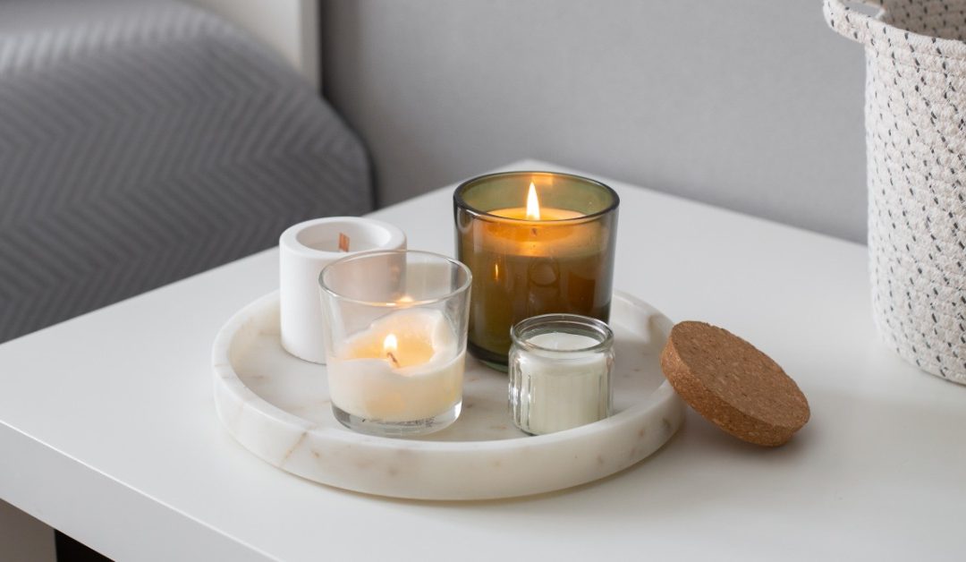 A close-up of a bedside table with a marble tray housing a few pillar candles of various heights. There's a basket nearby.
